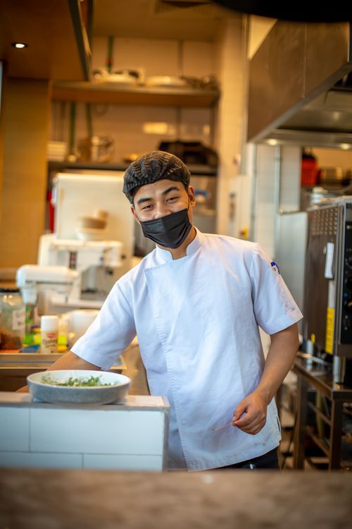 Free Portrait of a smiling chef wearing a face mask, preparing food in a Dubai kitchen. Stock Photo
