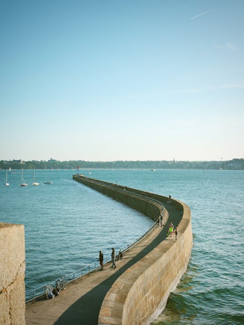 Free People Standing on Concrete Pier Jutting Out on Sea Under Blue Sky Stock Photo