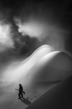 A lone worker navigates snowy terrain in Falun, Sweden, creating a dramatic black and white scene.