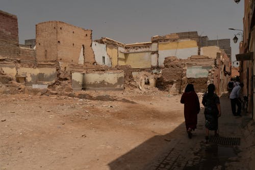 People Walking Near Abandoned and Ruined Buildings on Dirt Ground
