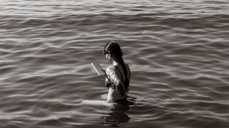 Woman Standing In Water And Reading A Book 