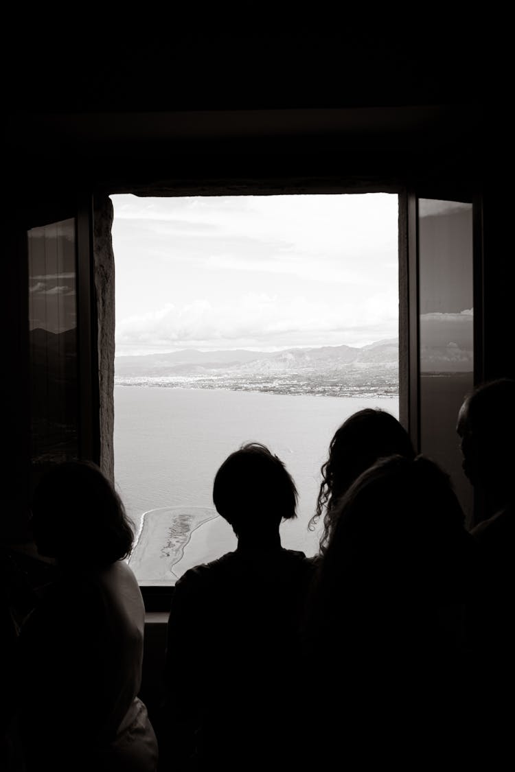 Silhouette Of People Standing In Front Of A Window Looking At The Sea