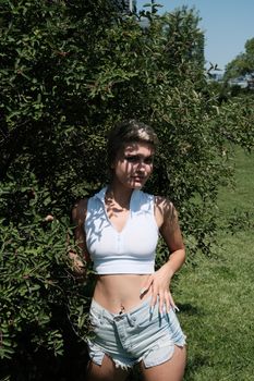 Chic young woman poses confidently outdoors in summer attire, blending elegance and nature.