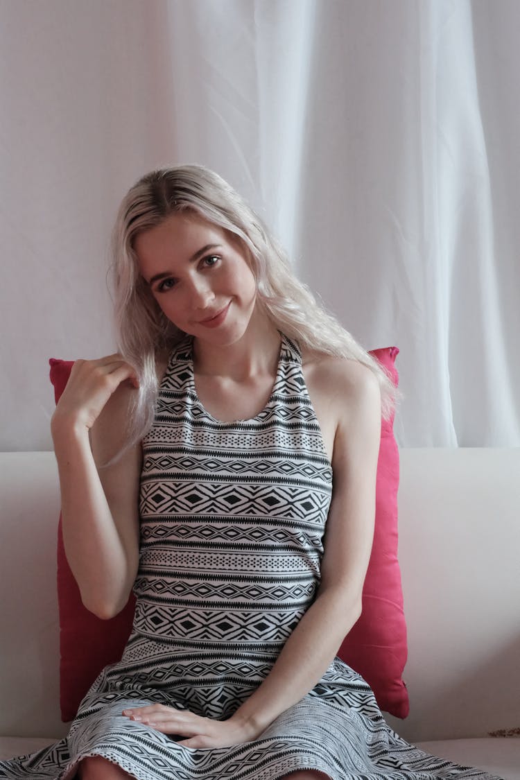 Woman In Black And White Sleeveless Dress Sitting On Couch With Pink Pillow