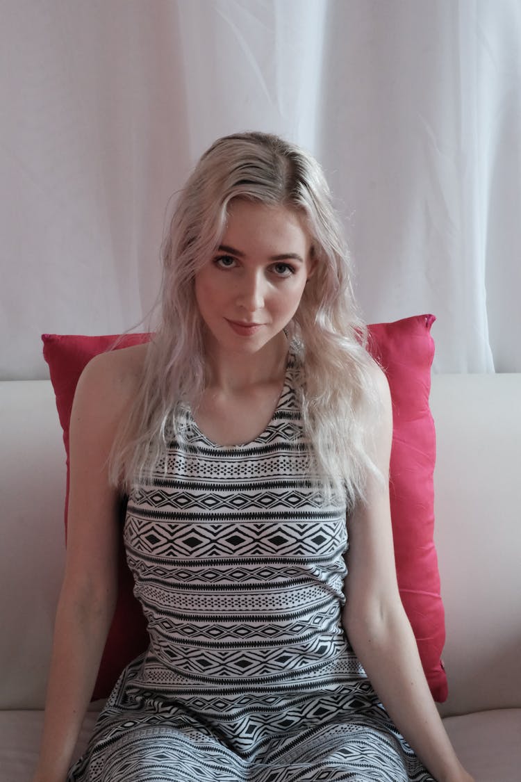 A Beautiful Woman Sitting On A Couch While Leaning On Pink Throw Pillow