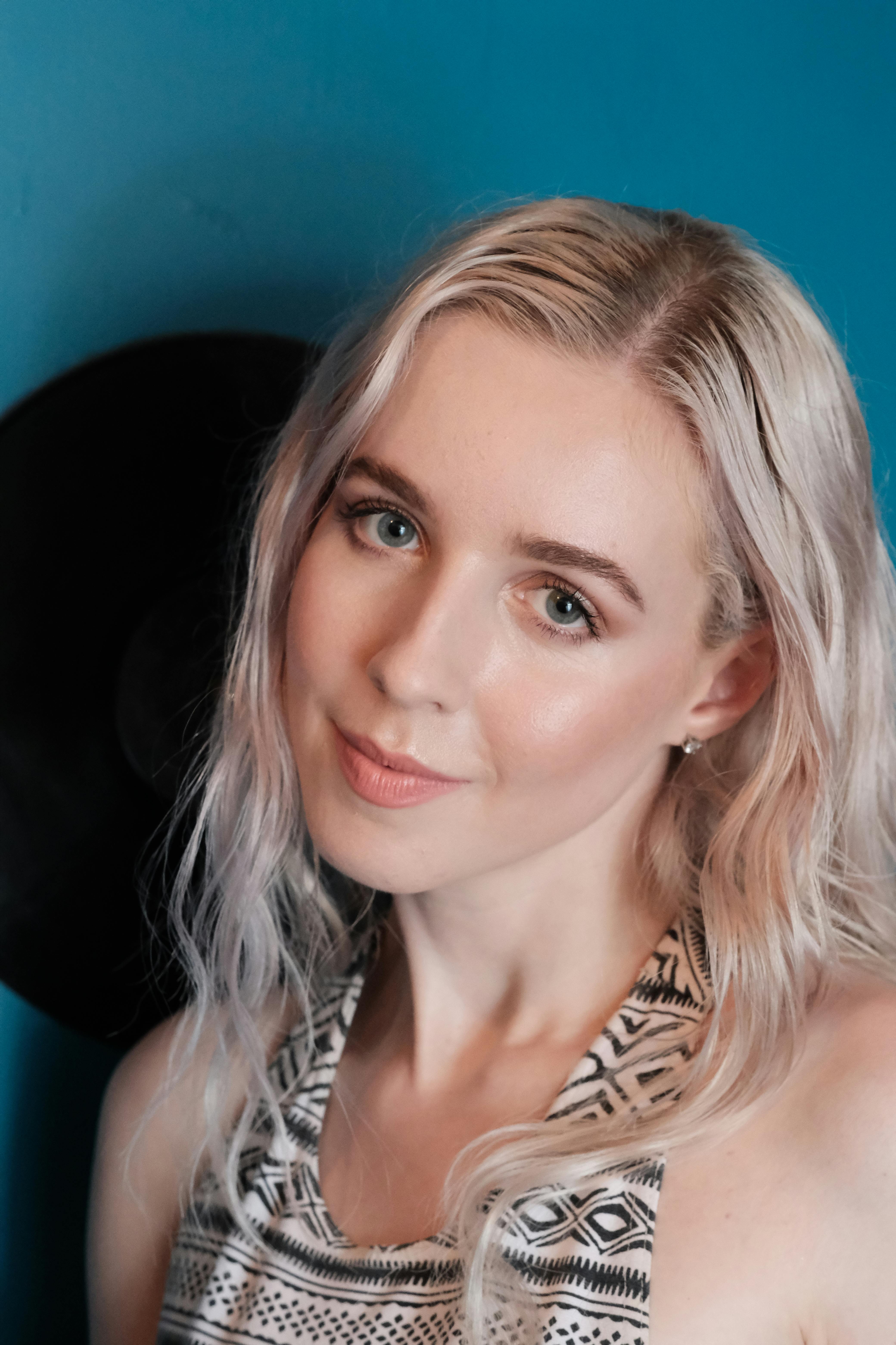 Close-up portrait of a blonde woman in tribal-patterned top, blue background.