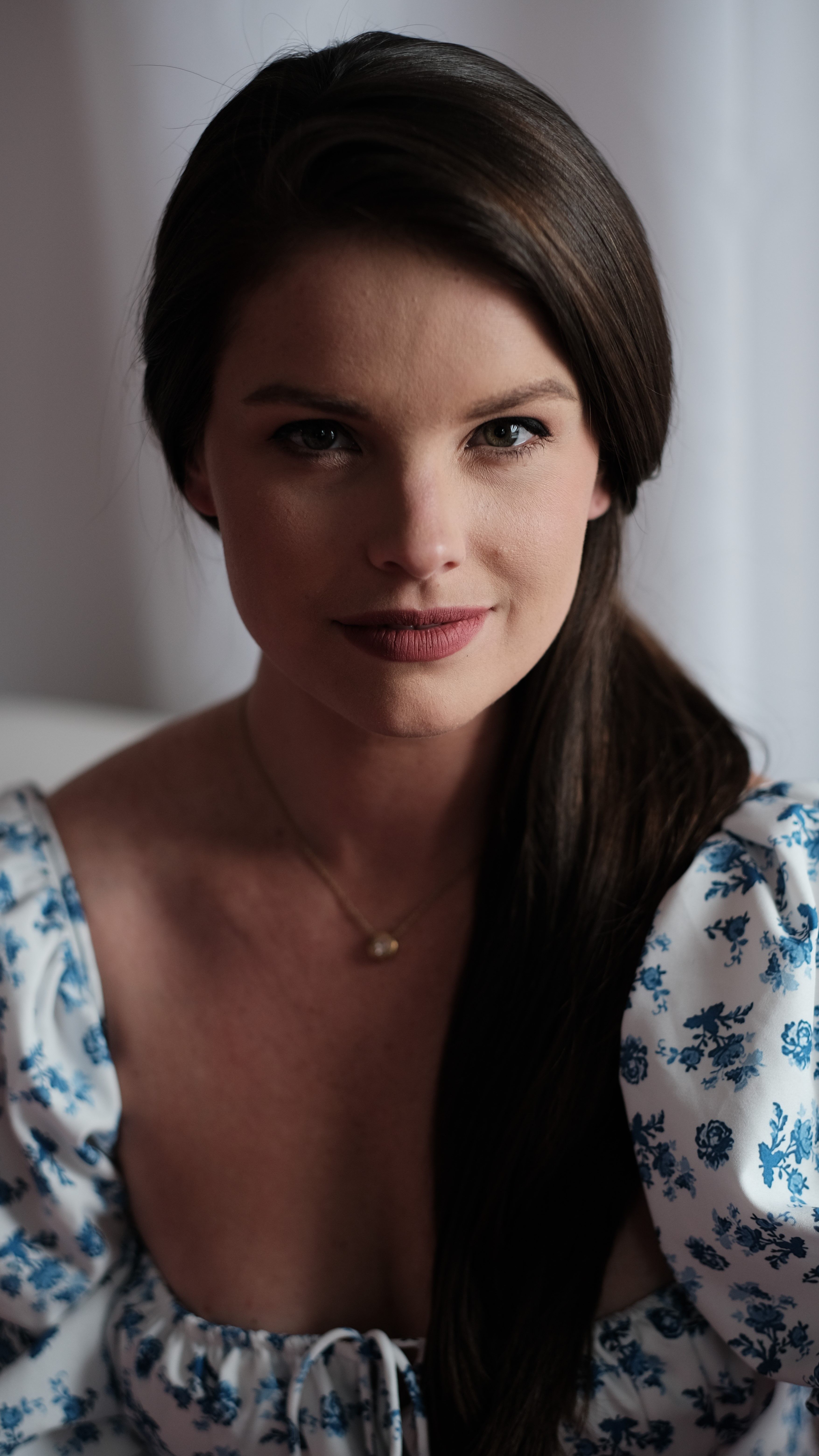 Sophisticated portrait of a young woman with long dark hair in a floral dress, exuding grace.
