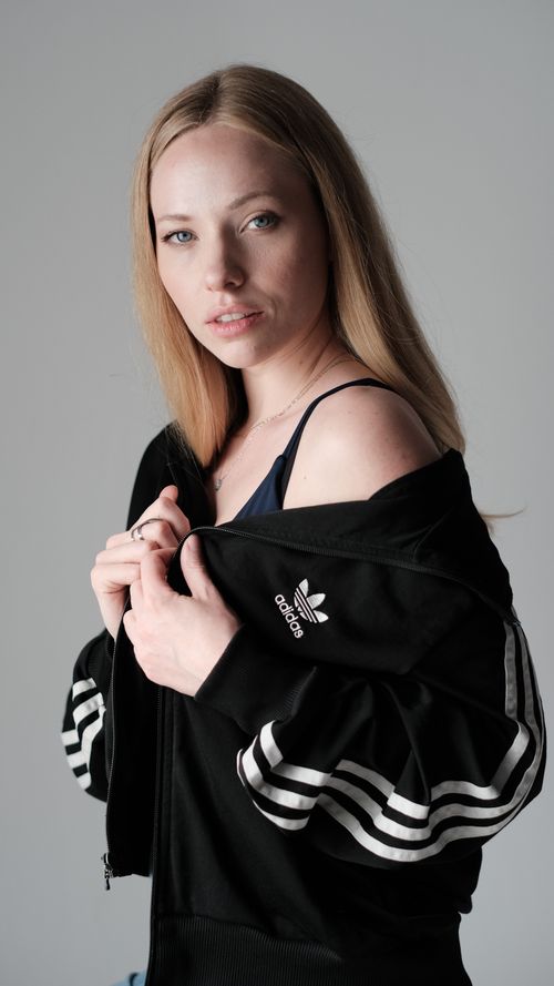 Free Young woman posing in studio wearing an Adidas jacket, exuding a casual and stylish look. Stock Photo