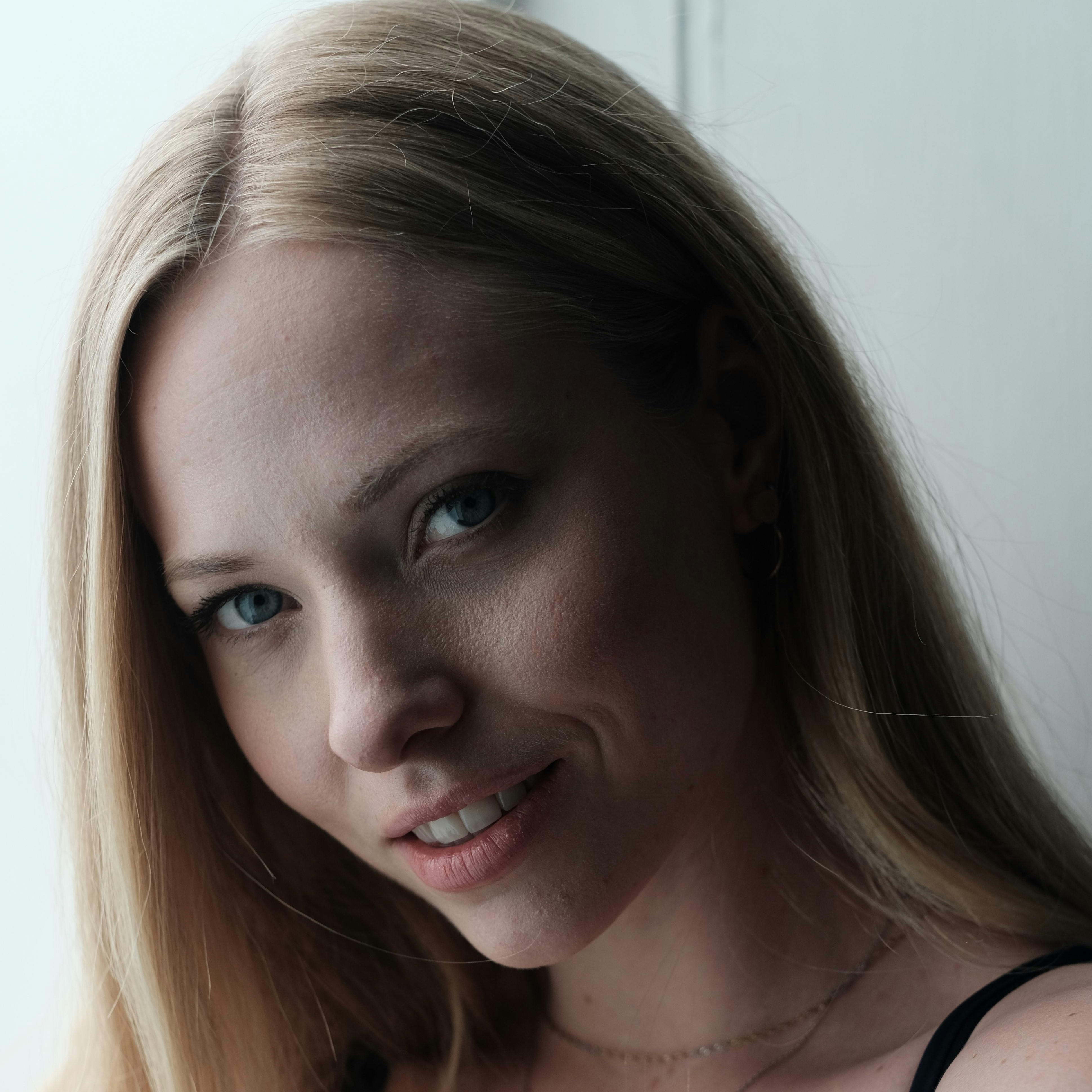 Portrait of a smiling woman with blonde hair, captured in soft natural light indoors.