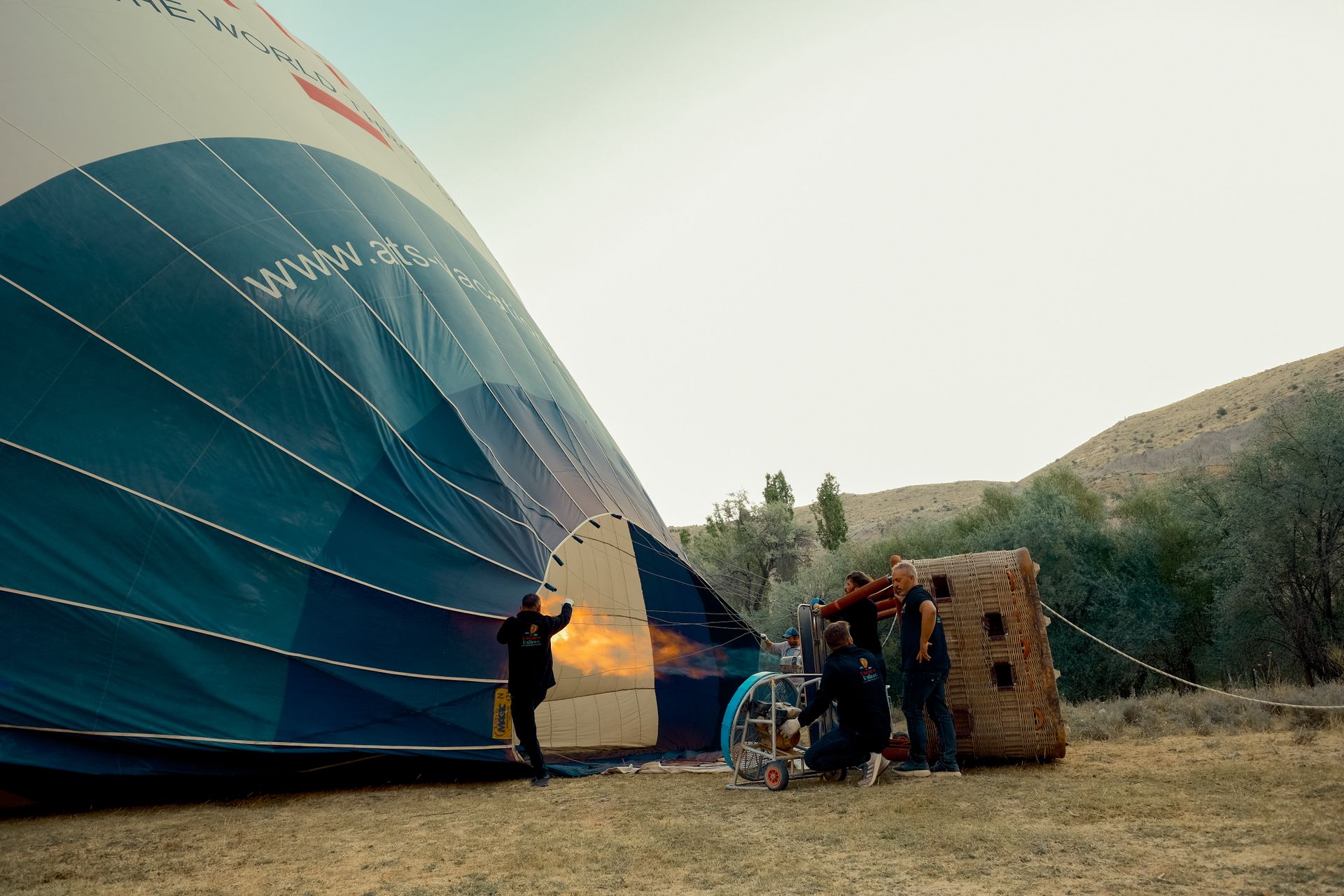 Crew inflating hot air balloon with flame outdoors, readying for scenic adventure flight.