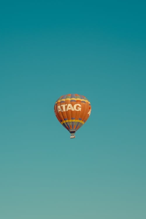 A White and Orange Hot Air Balloon in Mid Air Under Blue Sky