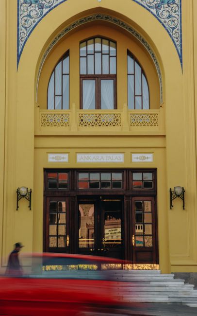 A blurry red object passes by the ornate entrance of the historic Ankara Palace in Turkey.