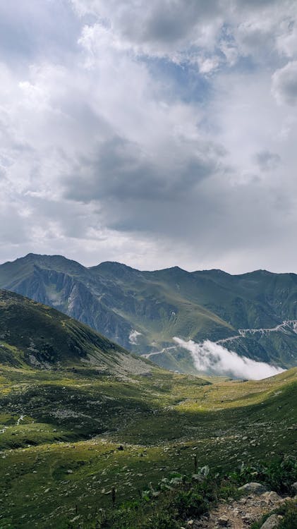 Landscape of Grass Field in Mountains and Mountain Range under a Cloudy Sky 