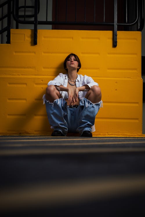 Young Woman in a Trendy Outfit Crouching Against a Wall in City 