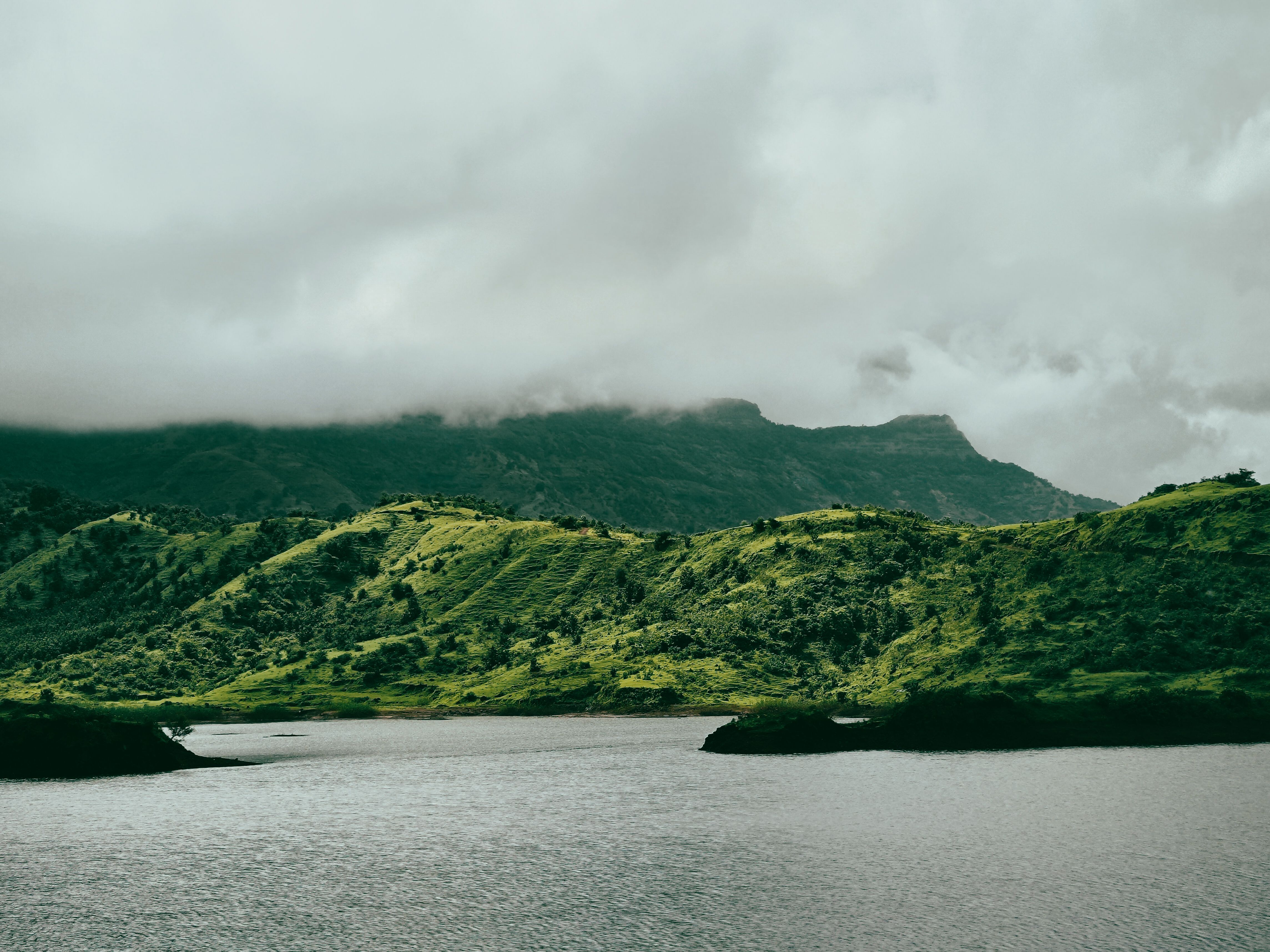 Scenic landscape of lush green hills and a calm lake beneath overcast skies.