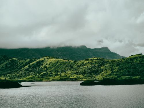 Free Scenic landscape of lush green hills and a calm lake beneath overcast skies. Stock Photo