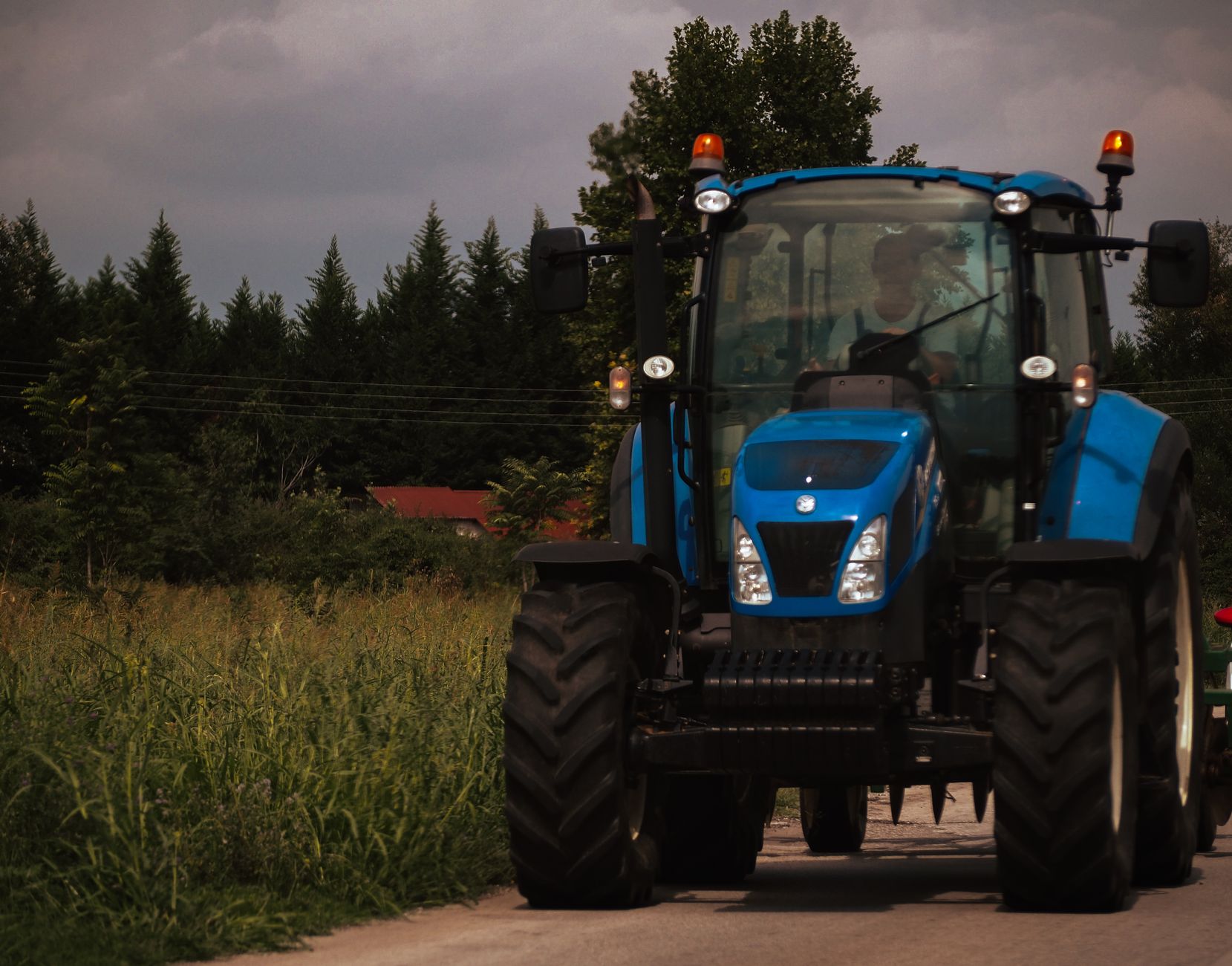 A blue tractor navigates a rural road surrounded by greenery, highlighting agricultural activity.