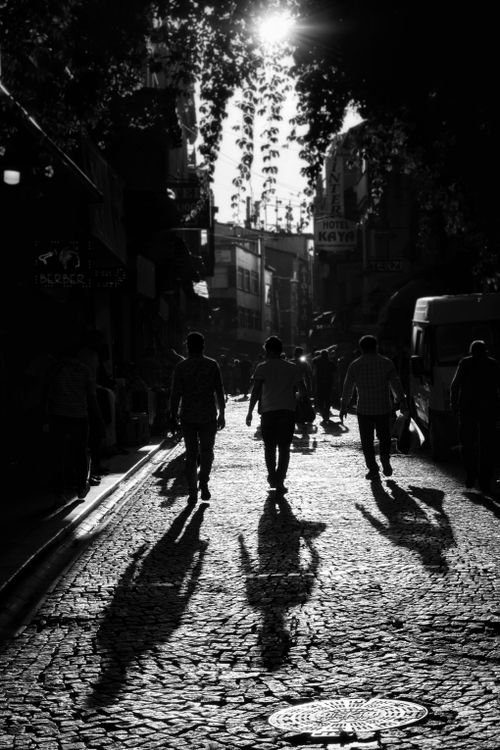 Free Black-and-white scene of people walking down a sunlit cobblestone street. Stock Photo