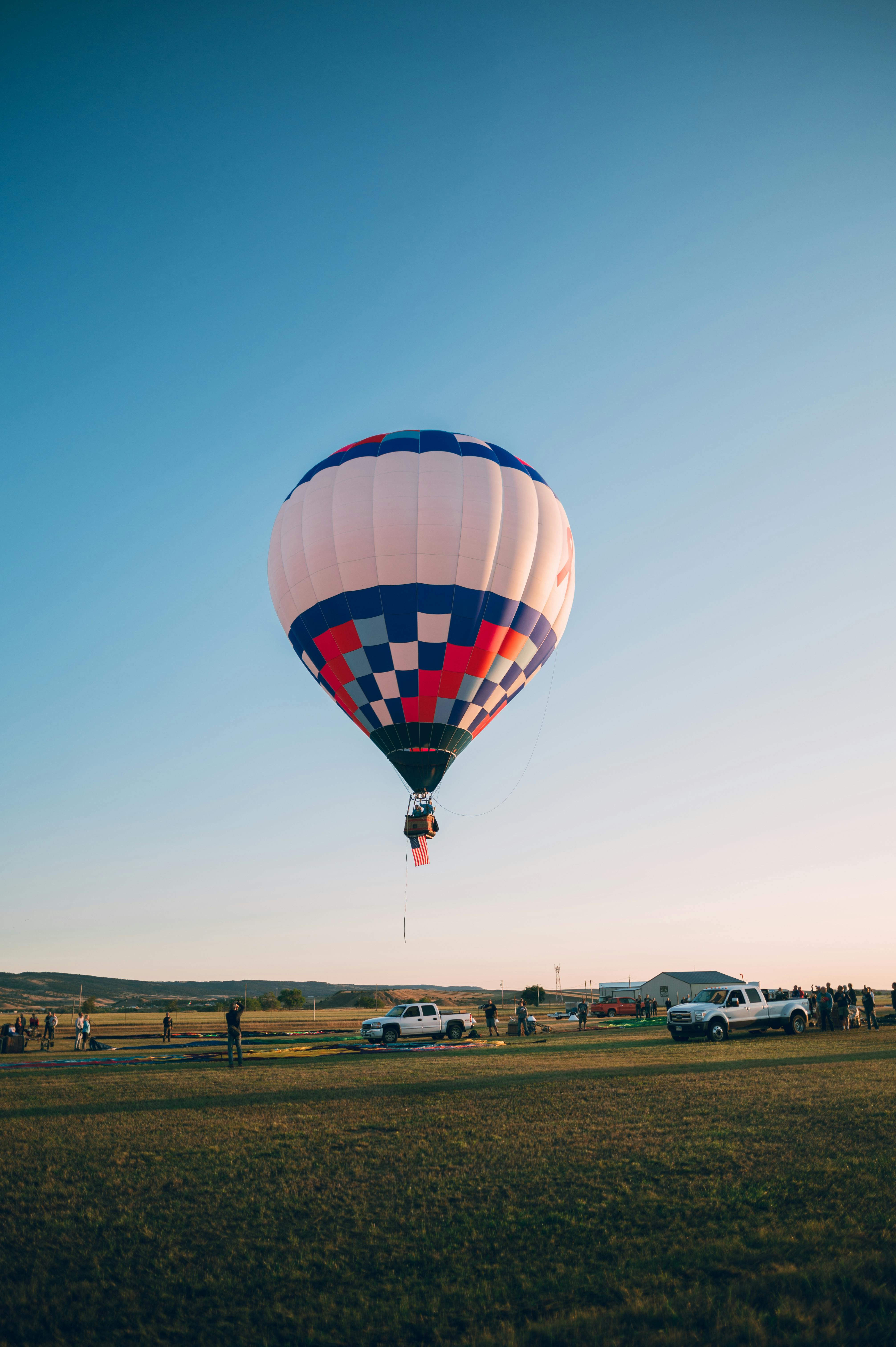 Vibrant hot air balloon soaring above an open field with spectators watching during sunset.