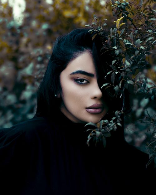 Free Elegant portrait of a woman partly concealed by leaves, evoking mystery. Stock Photo
