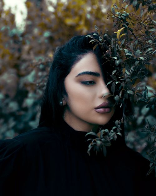 Free Portrait of a woman with dark hair partly covered by leaves in an outdoor setting. Stock Photo