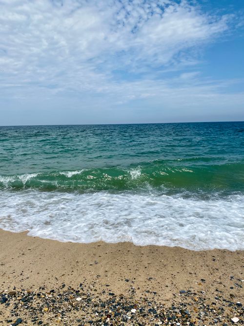 Free Peaceful beach scene with gentle waves lapping the shore under a vast blue sky. Stock Photo