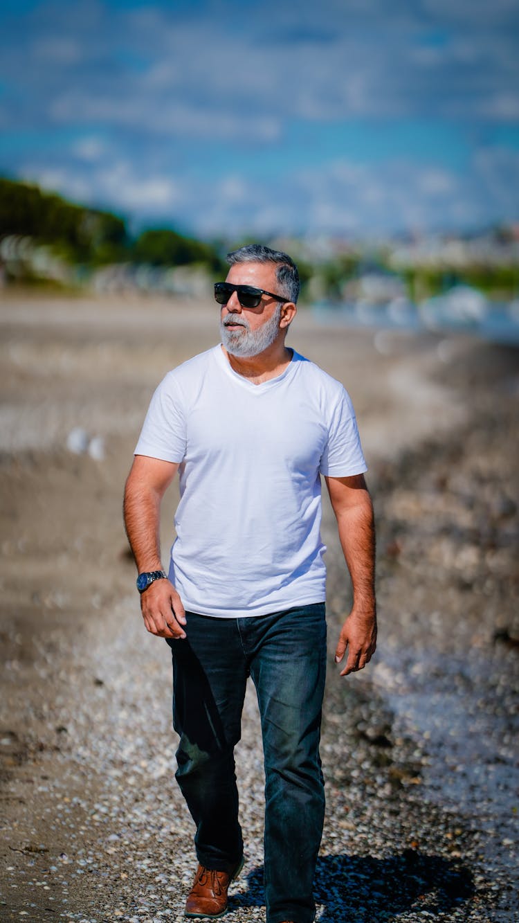 Man In White Crew Neck T-shirt And Black Denim Jeans Walking In Unpaved Ground 