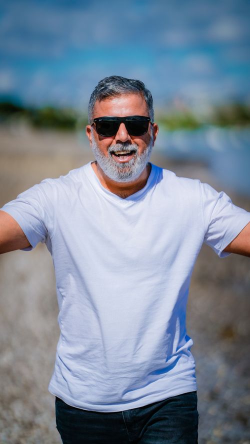 Free A cheerful middle-aged man with sunglasses smiles on a sunny Auckland beach, capturing a vibrant moment. Stock Photo