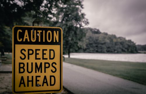 Free Yellow caution sign warning of speed bumps, placed in a park environment, overcast day. Stock Photo