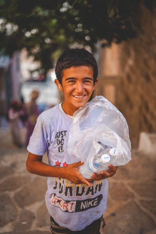 Free A cheerful boy holds plastic bottles while walking outdoors, showcasing a carefree moment. Stock Photo