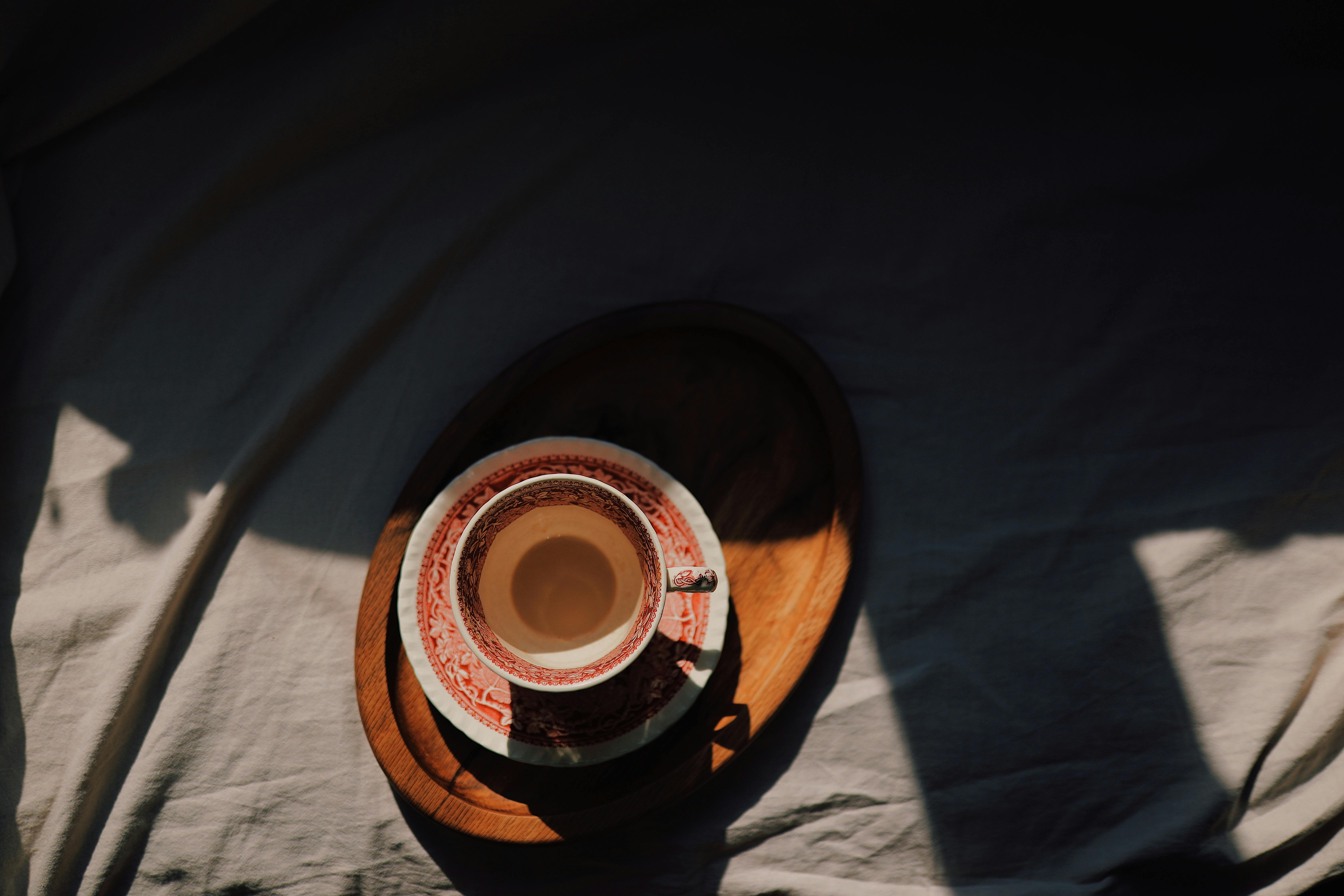 Artistic photo of a decorative cup and saucer on a wooden tray with dramatic lighting.