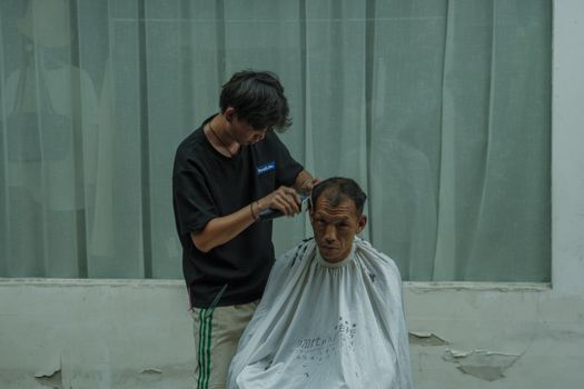 A hairdresser cuts a man's hair under natural lighting, creating a casual and relaxed atmosphere.