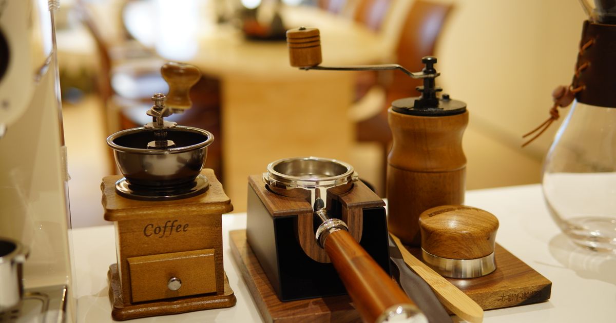 A wooden coffee grinder beside espresso tools on a kitchen counter