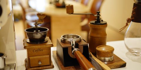 A wooden coffee grinder beside espresso tools on a kitchen counter