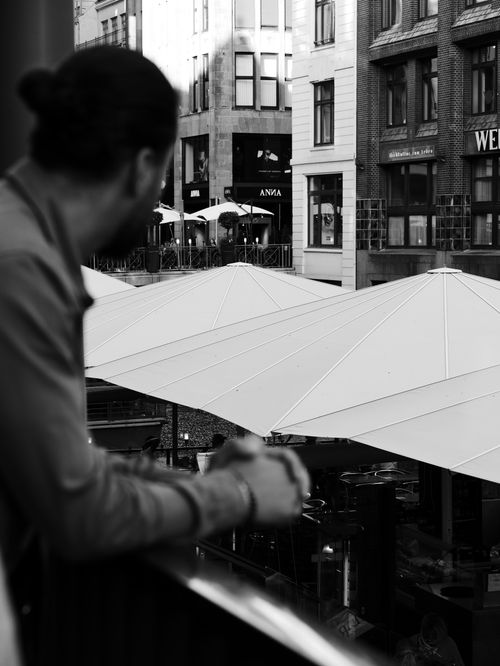 Free Man overlooking a lively urban scene with balconies and large umbrellas in a black and white setting. Stock Photo