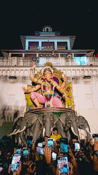 A lively scene of Ganesh Chaturthi celebration featuring a large Ganesh statue surrounded by a crowd taking photos.