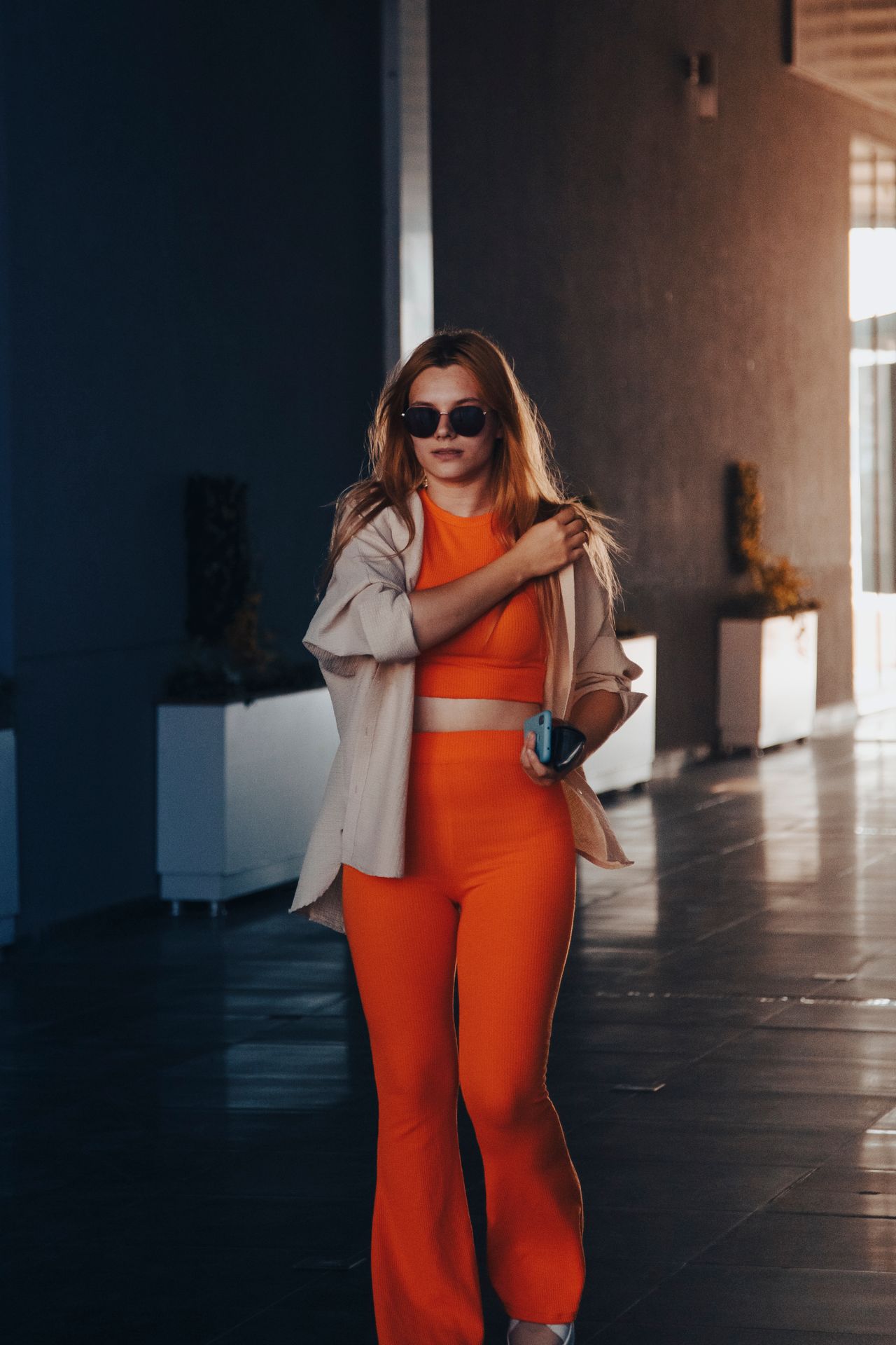 Woman in a bright orange matching knit set with an open shirt and sunglasses
