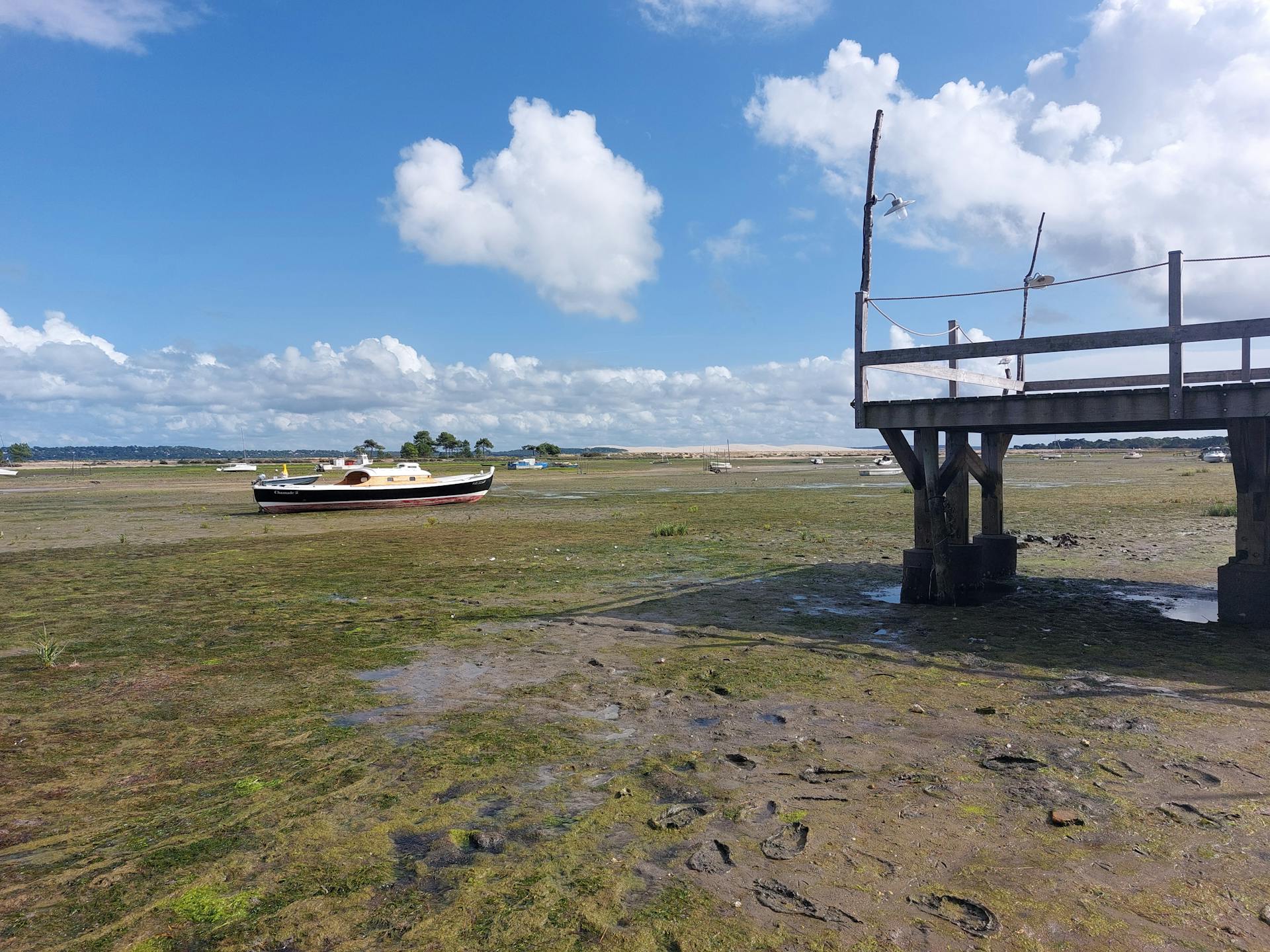 A boat stranded on dry land by a wooden dock during low tide on a sunny day.