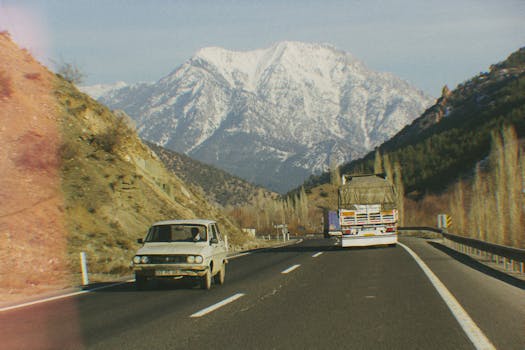 A nostalgic road scene with cars and trucks on a mountain highway, captured in film photography.