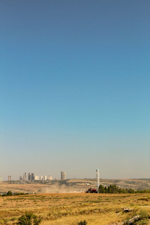 Free Expansive grassland with distant city skyline and drilling rig under a clear sky. Stock Photo