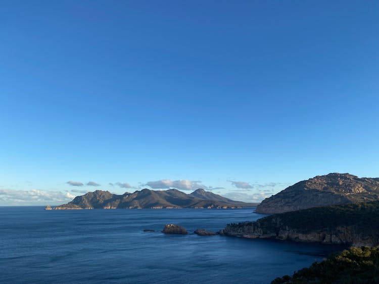 Blue Sea Near Mountain Under Blue Sky