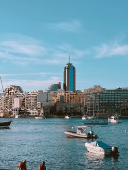 Urban skyline with high-rise buildings and boats, reflecting a bustling waterfront cityscape.