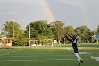 在阳光明媚的球场上，足球运动员跳跃接球，背景是充满活力的彩虹