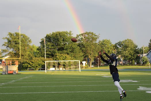 在阳光明媚的球场上，足球运动员跳跃接球，背景是充满活力的彩虹