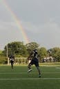 在鲜艳的彩虹下，两名足球运动员在球场上练习