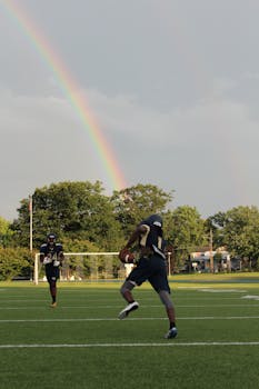 Two football players practicing on a field beneath a vivid rainbow.