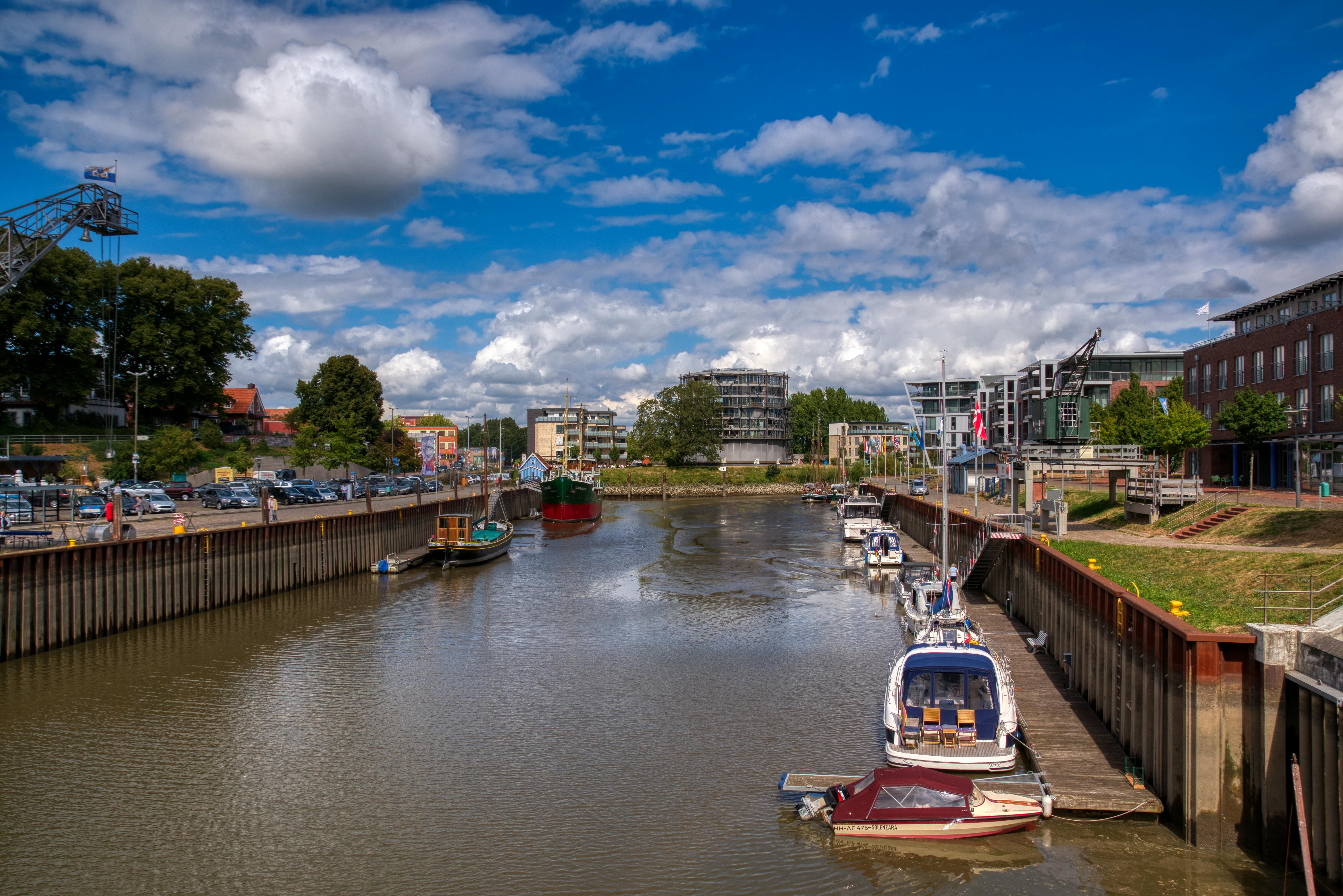 Scenic view of boats docked in a city canal, surrounded by buildings and trees under a vibrant sky.