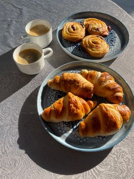 Fresh croissants with coffee cups on sunlit table, perfect morning treat.