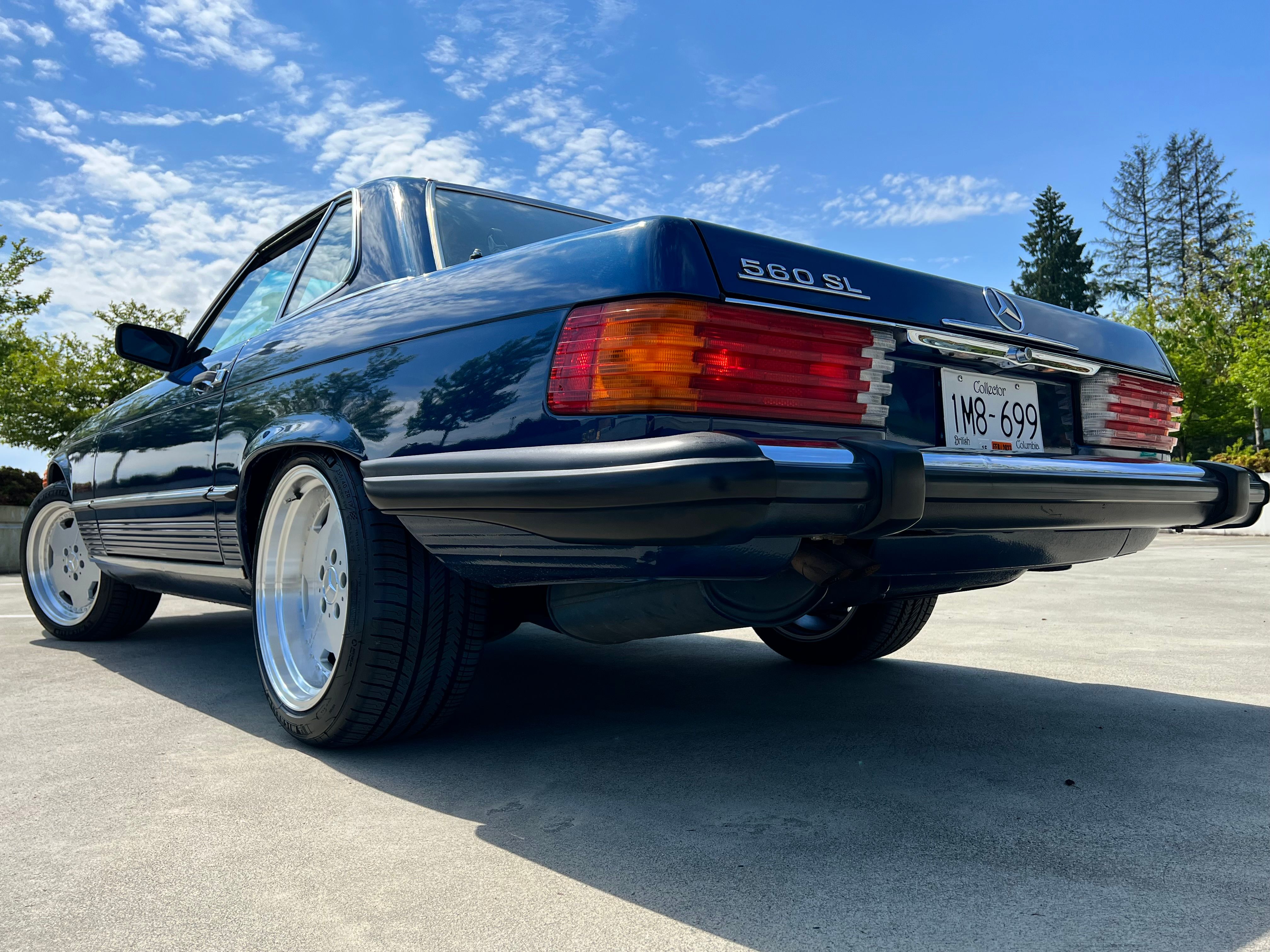 Vintage Mercedes-Benz 560 SL parked under clear blue sky, showcasing sleek design and chrome details.