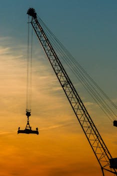 A tower crane silhouette set against a vibrant orange sunset sky in Reykjavík, Iceland.